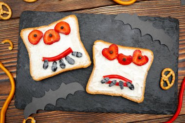 Cadılar bayramında kızarmış ekmek, tereyağı, çilek, şeker, servis masası, siyah arka planda yarasalar. Çocuklar için tatlı öğle yemeği..