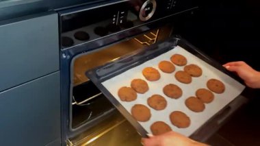 Genç bir kadın çarşaf yerleştiriyor, alıyor, ev mutfağındaki elektrikli fırına bir tepsi zencefilli kurabiye koyuyor. Ev yapımı ve yemek hazırlama.