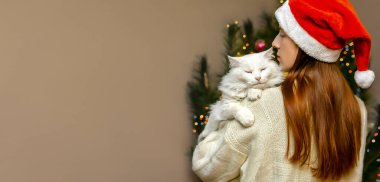 Noel Baba şapkalı kadın evde şirin kediye sarılıyor. Mutlu Noeller, evcil hayvanlarla, ailelerle yeni yıl tatili. Kutlama afişi için hazırlıklar.