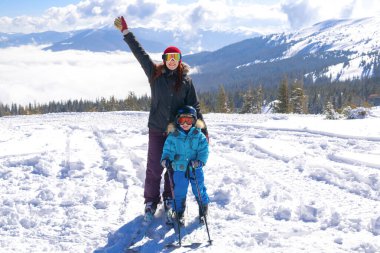 Genç sporcu kadın dağlarda kayak yapan çocukla kayak yaparken eğleniyor. Küçük anne oğul ailesi ekstrem spor aktivitelerinin tadını çıkarıyor.