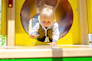 Küçük tatlı sarışın çocuk tünelden sürünerek geçiyor, çocuk parkında pipo içiyor. Çocukların fiziksel gelişimi ve çocuk yuvası, anaokulu kavramı
