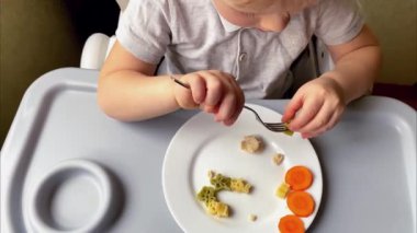 Bebek çocuk, çatal, el, kendini besleyen sebzeler, mutfakta tabak makarna yemeyi öğreniyor. Çocuklar sağlıklı beslenme konsepti geliştiriyor.