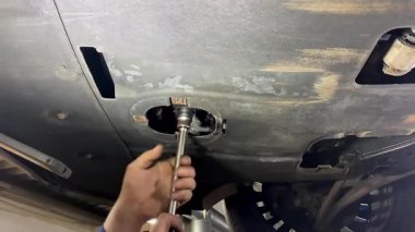 Tamirci arabanın altındaki motor filtresini yenisini değiştirmek için kaldırdı. Rutin bakım kontrolü, oto tamirhanesinde, garajda, araç servis istasyonunda boşa harcanan yağ