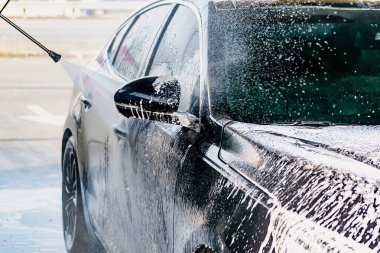 Yüksek basınçlı su jeti olan, otomatik oto yıkamada ekipman pompalı, köpüklü kimyasal deterjan kaplı bir araç.