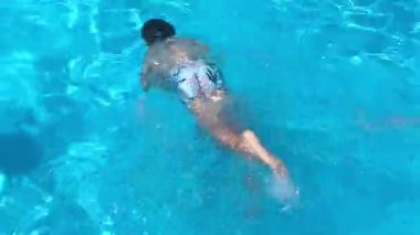 Küçük çocuk havuzda yüzüyor, çocuk yüzmeyi öğreniyor, suya dalıyor, oynuyor, eğleniyor. Yaz tatili, otelde aile tatili, turistler.