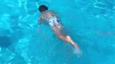 Küçük çocuk havuzda yüzüyor, çocuk yüzmeyi öğreniyor, suya dalıyor, oynuyor, eğleniyor. Yaz tatili, otelde aile tatili, turistler.