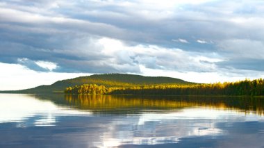 Vahşi orman, göl kıyısında güneşin batışıyla aydınlanır.