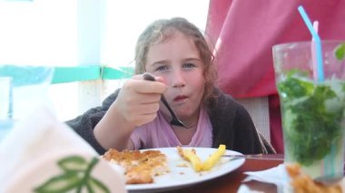 Çocuk meyve suyu içiyor ve yaz tatilinde masada patates kızartması yiyor.
