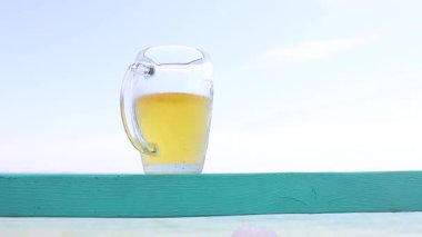 Su kenarında bir bardak bira, arka planda deniz, yaz tatili.