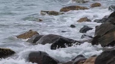 Dalgalar engebeli bir kıyı şeridi boyunca kayaların üzerinden kırılıyor.