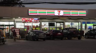 Müşteriler 7-Eleven mağazasına girip çıkıyorlar.