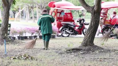 Motorsiklet ve bankın yanında yaprakları tırmıklayan işçiler.