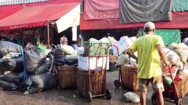 İşçiler kalabalık bir açık hava pazarında mal taşıyorlar