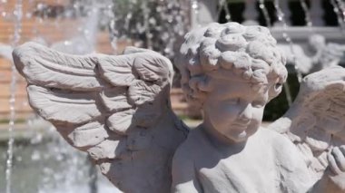 Su çeşmesinin yanında kanatları olan bir melek heykeli.