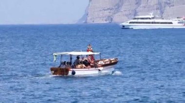 Kayalıkların ve yatların yanında turist teknesi geziyor.