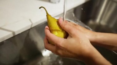 Eller akan suyun altında armut yıkıyor.