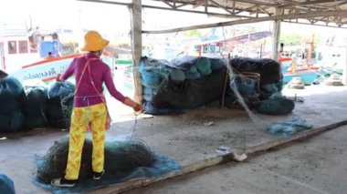 Deniz kıyısındaki bir rıhtımda balık ağları düzenleyen kişi