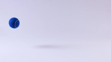 Mavi bir tenis topu beyaz yüzeyde zıplıyor.