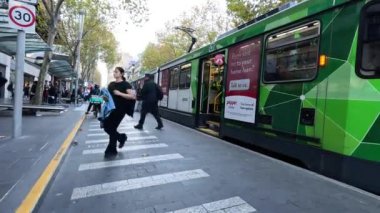 İnsanlar yeşil tramvay yakınında karşıdan karşıya geçiyor.