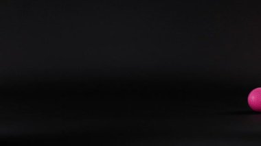 Pembe bir top karanlık bir yüzeyde yuvarlanıyor.