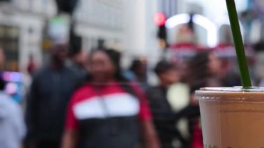 Kalabalık bir caddede insanlar bir içkinin yanından geçiyor.