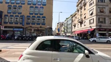 Milano caddesi kavşağında araçlar ve yayalar var.