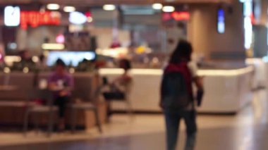 İnsanlar kalabalık bir lokantada yürüyüp yemek yiyorlar.