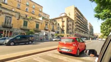 Arabalar ve yayalar hareketli bir Napoli caddesinde yol alırlar.