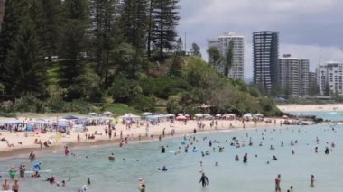 Arka planda şehir silueti olan kalabalık plaj sahneleri