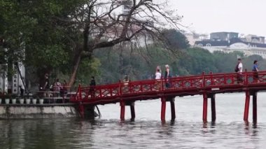 İnsanlar suyun üzerinden kırmızı bir köprüden geçiyor.