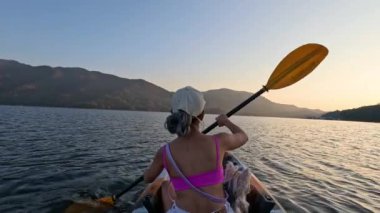 Gün batımında gölde kayak yapan biri.