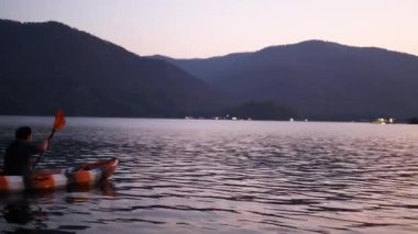 Alacakaranlıkta sakin bir gölde iki kişi birlikte kano yapıyor..