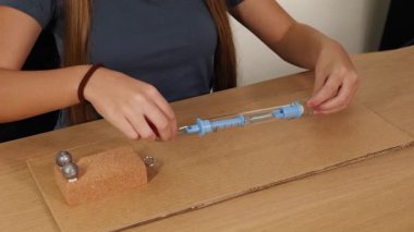 Eller, sürtünme ve ağırlık dinamiğini gösteren karton yüzeydeki kuvveti ölçmek için bir yay ölçeğini manipüle eder.