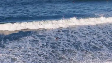 Sörfçüler Gold Coast, Avustralya 'da açık gökyüzünün altında güçlü dalgalara binerler. Canlı mavi ve beyaz zıtlıklarla dinamik okyanus sahnesi