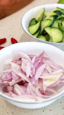 İyi aydınlatılmış bir mutfakta ahşap bir tahtada salatalık, arpacık soğanı ve biber de dahil olmak üzere sebze doğramak.