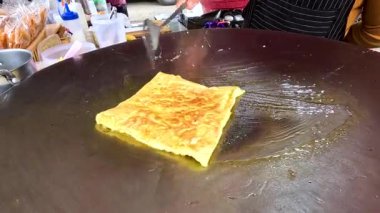 Bir sokak satıcısı Tayland, Kanchanaburi 'de büyük bir ızgarada kızartılmış roti pişiriyor. Parlak ışıklandırma altın-kahverengi dokusunu vurgular