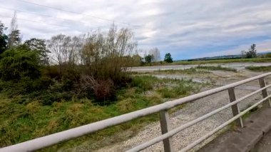 Tekapo Gölü 'ndeki bir köprünün üzerinden sakin bir sürüş, yemyeşil ve geniş gökyüzünü yumuşak, dağınık ışık altında yakıyor.