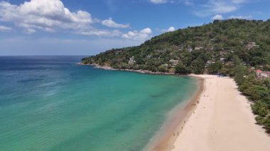 İnsansız hava aracı görüntülerinde Phuket, Tayland 'da sakin bir sahil görülüyor. Açık gökyüzü altında turkuaz sular, kumlu kıyılar ve yemyeşil alanlar sergileniyor.