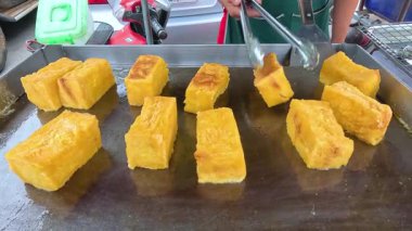 Bir sokak satıcısı Tayland, Kanchanaburi 'de sıcak bir ızgarada tereyağlı ekmek pişirmek için maşa kullanıyor. Parlak ışıklandırma altın dokuyu vurgular