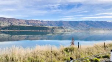 Queenstown, Yeni Zelanda 'da berrak bir gökyüzünün altında dağ yansımaları olan sakin bir göl kenarında sakin bir yolculuk.