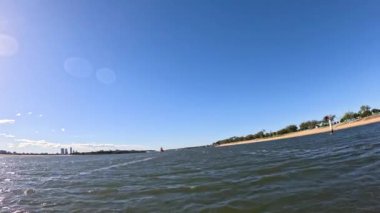 Açık mavi gökyüzünün altında dalgalar ve kıyı şeridi