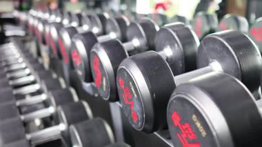 İyi aydınlatılmış bir spor salonunda, spor salonundaki dambıllar, spor ve güç eğitimini ön plana çıkarıyor. Kamera ekipmanları çeşitli açılardan yakalar.