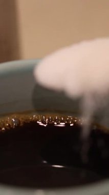 Bir kaşık dolusu şeker dumanı tüten bir fincan kahveye eklenir ve sıvı içinde girdap etkisi yaratır.