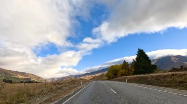 Wanaka, Yeni Zelanda 'da dolambaçlı bir yol boyunca sakin bir sürüş canlı bir sonbahar yeşilliği ve geniş gökyüzü sergiliyor.