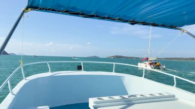 Bir tekne, Chalong Körfezi, Phuket 'teki berrak gökyüzünün altında turkuaz sularda süzülerek sakin okyanus manzaralarını ve uzak adaları yakalıyor.