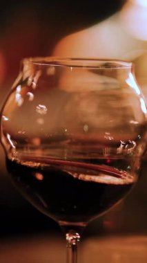 Kırmızı şaraplı bir şarap kadehi sıcak, çevresel aydınlatmada nazikçe kıvrılır, sofistike ve samimi bir atmosfer yaratır.