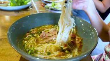 Bir insan yemek çubuklarını lezzetli bir Vietnam çorbasından erişte kaldırmak için kullanır. Sıradan bir yemek ortamında hazırlanır.