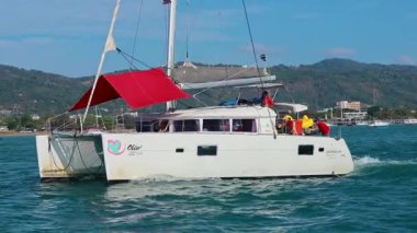 Kızıl yelkenli bir katamaran, Tayland 'ın Phuket yakınlarındaki turkuaz sularda süzülüyor. Parlak gün ışığında, dağ zemininde.