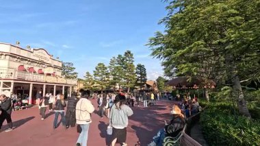 Ziyaretçiler açık gökyüzünün altında Tokyo Disneyland 'da yürüyorlar. Canlı sahne canlı atmosferi ve ikonik mimariyi yakalıyor.