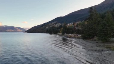 Hava görüntüleri Wakatipu Gölü 'nün kıyı şeridini, yemyeşil ve yumuşak gün ışığı altında uzak dağlarla çevrili huzurlu bir şekilde yakalar.